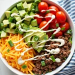 Low-carb easy Keto taco bowl with seasoned ground beef, avocado, shredded cheese, lettuce, tomatoes, and sour cream in a bowl